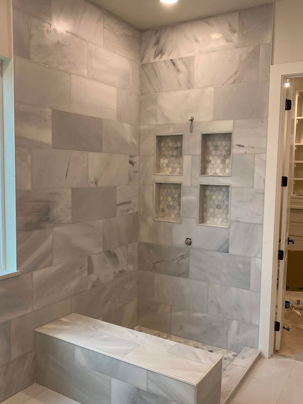 Marble-look porcelain tile shower with hexagon mosaic niche shelves in a Granbury, TX bathroom remodel