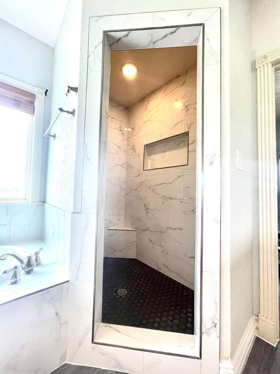 Walk-in marble-look tile shower with built-in bench and black pebble tile floor in a Glen Rose, TX home