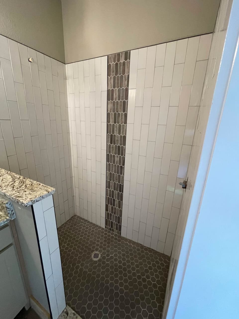 White vertical subway tile shower with hexagon mosaic accent band in a Granbury, TX bathroom